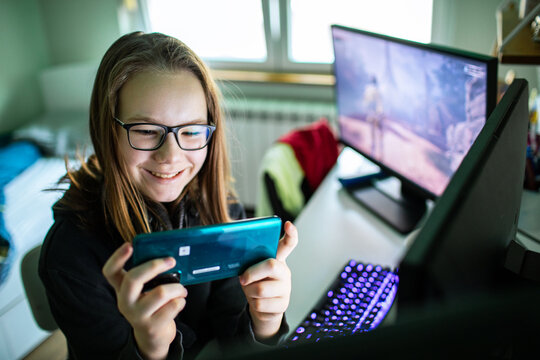 Smiling teen girl gaming on smartphone at home desk