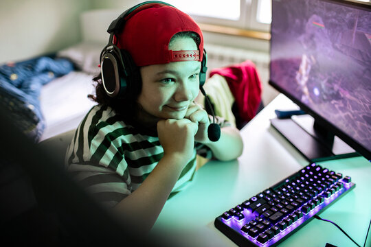 Smiling child gamer with headset playing computer at home bedroom