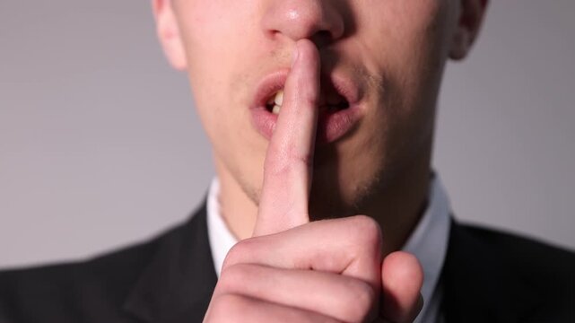 Businessman showing hush gesture on grey background, closeup