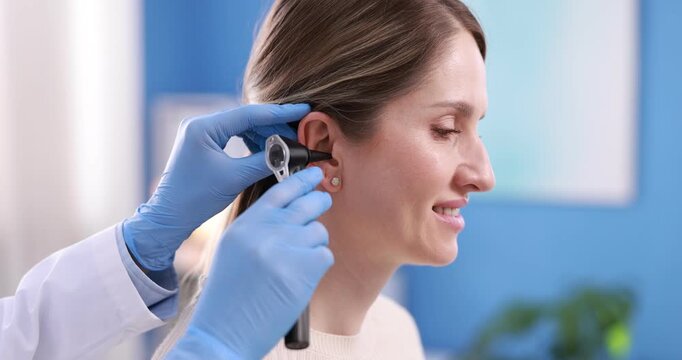 Hearing test. Doctor examining woman's ear with otoscope in clinic, closeup. Camera spinning and moving forward