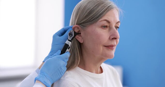Hearing test. Doctor examining woman's ear with otoscope in clinic, closeup