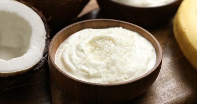 Adding coconut flakes to yogurt at wooden table, closeup