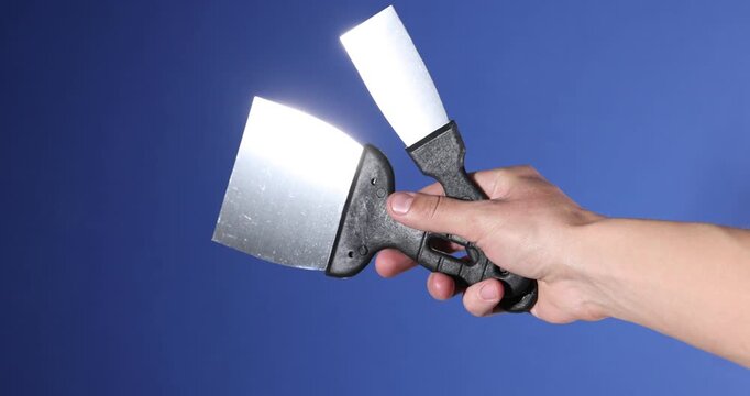 Handyman with putty knives on blue background, closeup