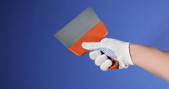 Handyman with putty knife on blue background, closeup