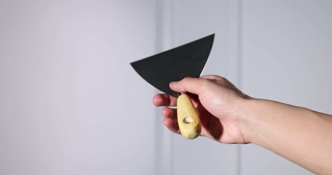 Handyman with putty knife on light background, closeup