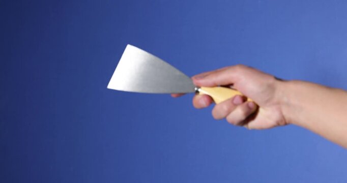 Handyman with putty knife on blue background, closeup