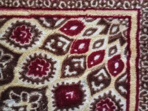 Traditional Ornamental Carpet Close Up Texture. 
Traditional patterned carpet featuring intricate floral and geometric motifs in rich red, cream, beige, and brown tones with soft textured woven fabric
