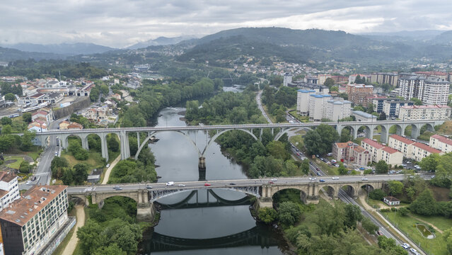 Aerial view of the Ponte Nova bridge and railway viaduct crossing the Minho River surrounded by lush green trees and urban buildings in Orense, Ourense, Spain.