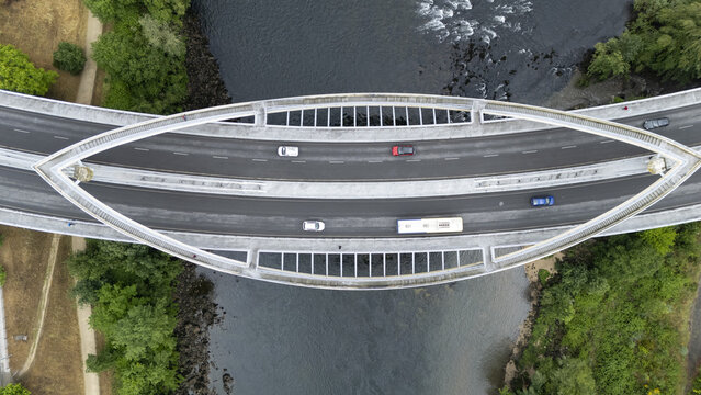 Aerial view of Ponte do Milenio bridge crossing the river with cars and a bus on the asphalt road surrounded by green trees Orense, Ourense, Spain.