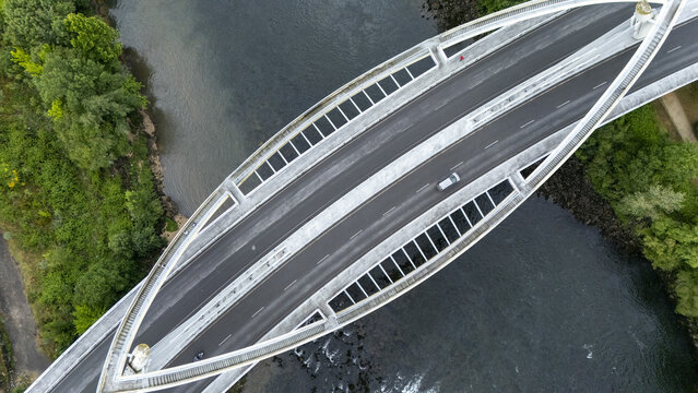 Aerial view of the modern Ponte do Milenio bridge with its unique pedestrian walkway crossing the Minho River surrounded by lush green trees Orense, Ourense, Spain.