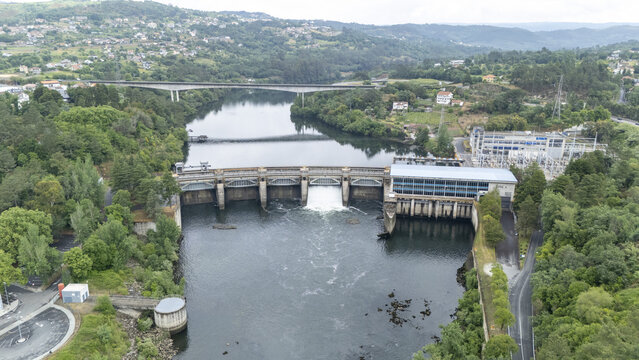Aerial view of the Velle Hydroelectric Power Station and dam on the Mino River with lush green hills and a bridge in the background Ourense, Ourense, Spain.