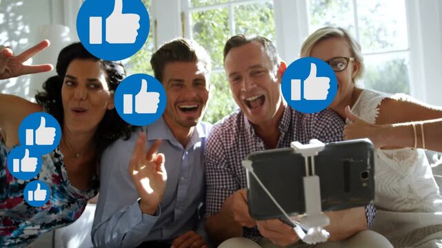 Four adults posing for social selfie, holding phone stick, animated blue thumbs-up covering faces