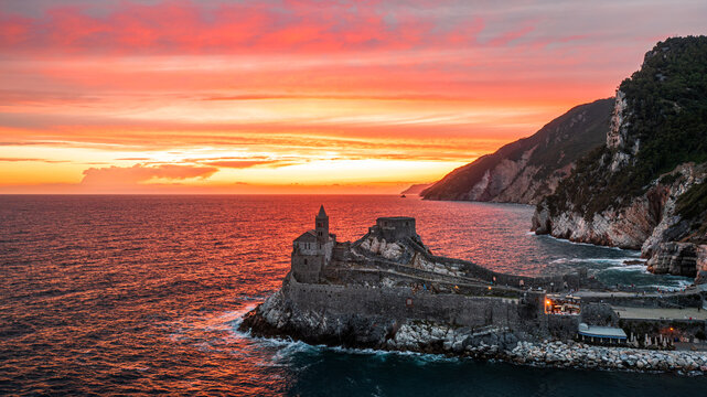 Aerial view of Chiesa di San Pietro on a rocky cliff overlooking the sea during a vibrant sunset in Portovenere, Liguria, Italy.