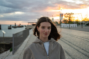 Obraz premium Young woman stand near water at sunset, casual urban fashion, vibrant sky, natural light, outdoors lifestyle