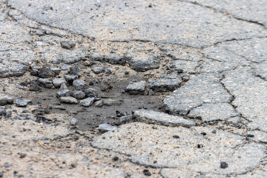 La Tuque, Canada, 01 May 2026 : Close-up view of a damaged asphalt road surface with cracks, loose gravel, and a pothole.
