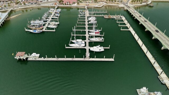 Aerial view of boats docked at a marina next to a bridge and urban shoreline with green water in St. Augustine, Florida, United States.