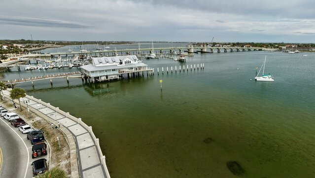 Aerial view of the Bridge of Lions spanning the Matanzas River with boats docked near the historic waterfront and a white building on stilts in St. Augustine, Florida, United States.