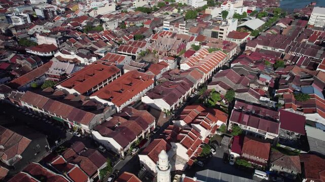 Cinematic drone push forward over Georgetown Penang revealing a mosque minaret and nearby Chinese temple surrounded by dense red roof buildings.