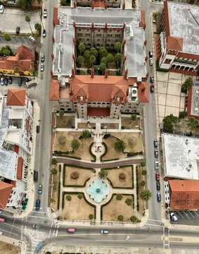 Aerial view of the historic Flagler College building featuring red-tiled roofs, a central courtyard with palm trees, and a formal garden with a fountain in St. Augustine, Florida, United States.