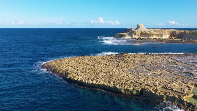Xwejni Salt Pans With Qolla l-bajda Rock In The Background Along The Coast of Gozo Island, Malta. Aerial Shot