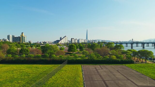 Aerial rise above Hangang Drone Park reveals Gwangnaru Hangang Park jogging tracks and riverside recreation with Lotte World Tower in Seoul's spring skyline Korea