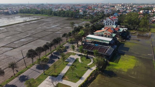 Aerial View Hoi An Rice Fields Sunlit Paddy Plots, Village Lane With Redtiled Roofs And Scattered Villas, Irrigation Canals Reflecting Sky, Dry Muddy Terraces And Distant Town Skyline,