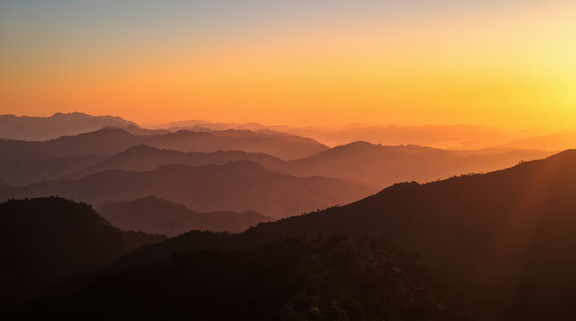Golden sunrise over layered mountain ridge with soft haze and warm glow