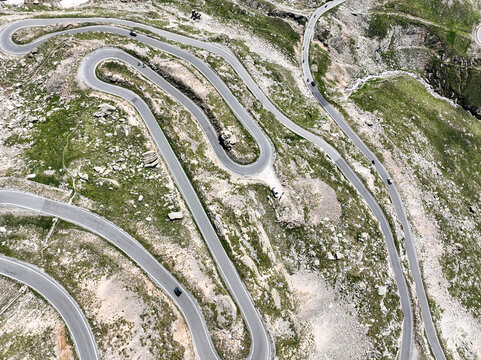 Aerial view of the winding mountain road at Colle del Nivolet with sharp hairpin turns and rocky alpine terrain in Valsavarenche, Aosta Valley, Italy.