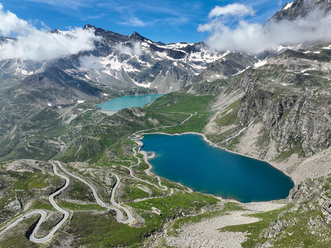 Aerial view of Agnel Lake and Serru Lake with the winding Colle del Nivolet road surrounded by snow-capped peaks and green slopes Ceresole Reale, Piedmont, Italy.