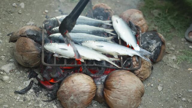 A person grilling milkfish (bangus) while adjusting the fire intensity.