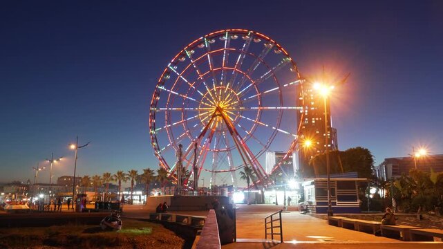 Timelapse of a spinning illuminated Ferris wheel on embankment in Batumi evening, sightseeing in Georgia, Adjara