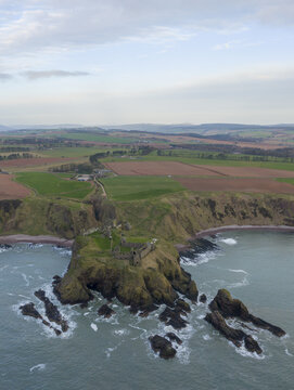 Aerial view of Dunnottar Castle perched on a dramatic rocky headland overlooking the North Sea with rolling green fields in the background Stonehaven, Scotland, United Kingdom.