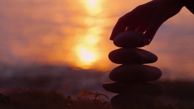 Zen stones balanced on a rocky shore at sunset, peaceful ocean backdrop with shimmering sunlight.