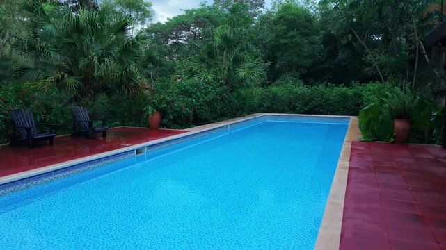 Outdoor swimming pool in Misiones Argentina surrounded by dense subtropical Atlantic Forest vegetation with tiled deck and lounge chairs, static shot