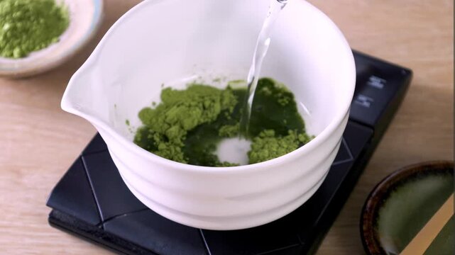Matcha green tea powder mixing with water in tea bowl by using chasen