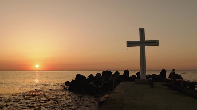 A serene ocean sunrise with a prominent cross on a pier, capturing the tranquility and spiritual essence of the morning light over the water.