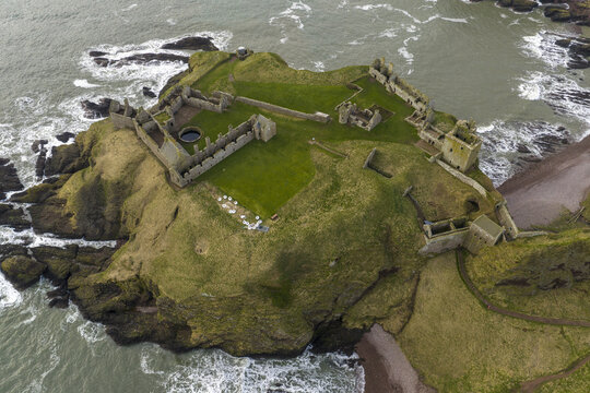 Aerial view of Dunnottar Castle ruins on a rocky cliff edge overlooking the North Sea with crashing waves and green grass Stonehaven, Scotland, United Kingdom.