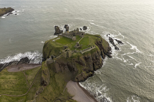 Aerial view of the medieval ruins of Dunnottar Castle perched on a dramatic rocky headland surrounded by the North Sea and steep cliffs in Stonehaven, Scotland, United Kingdom.