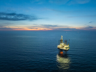 Obraz premium Aerial view from a drone of big jack up offshore drilling oil rig, production platform and supply vessel In the ocean during sunset - Oil and Gas Industry