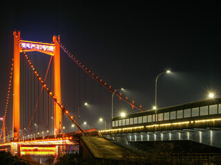Obraz premium Illuminated majestic red suspension bridge and elevated highway over river at night