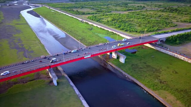 Cinematic Drone View of Red Arched Bridge Over River in Tropical City