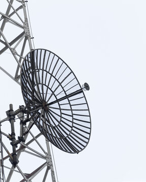 Closeup grid dish antenna attached to cellular communication tower with steel lattice framework, microwave reflector, feedhorn receiver, transmission support brackets and radio telecommunications