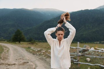 Obraz premium Cheerful woman outdoors, hair tied back, wearing a cozy sweater, relaxed pose in a countryside setting, soft breeze, natural light, calm atmosphere amid wide fields