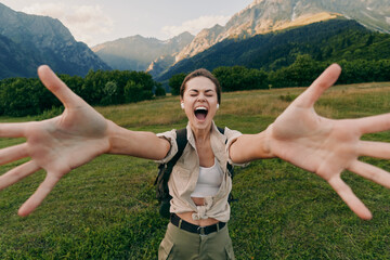 Naklejka premium Smiling woman with outstretched arms in a lush valley, mountains in the background. Lifestyle outdoors vibe, happiness, nature, adventure, and travel inspiration.