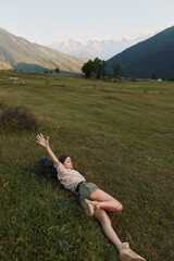 Fototapeta premium Relaxed woman lying on a grassy meadow with distant mountains, enjoying sunshine and fresh air, captured as a casual outdoor lifestyle moment in a natural landscape setting.