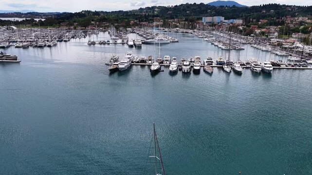 Aerial shot of a catamaran navigating through Gouvia Marina filled with luxury yachts and boats moored at pontoons in Corfu, Greece