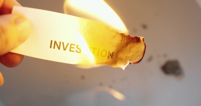 Close-up of paper labeled &ldquo;investment&rdquo; burning, symbolizing financial loss, risk, and decline in value.