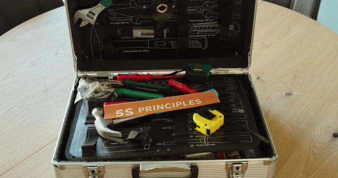 Hand holding &ldquo;5S Principles&rdquo; card over a toolbox, representing lean management methods for workplace organization and efficiency.