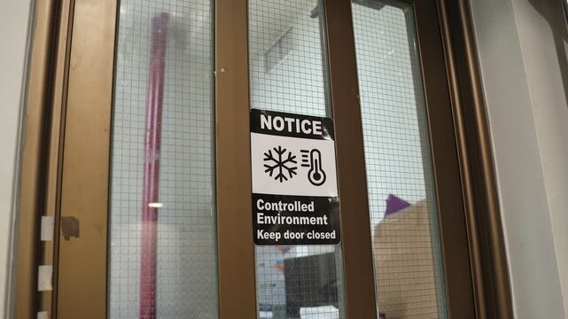 a notice sign on a reinforced glass door for a controlled environment. The label instructs personnel to keep the door closed to maintain strict temperature and climate settings.