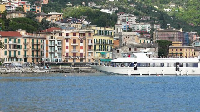 Vibrant waterfront scene in Rapallo, Italy with colorful historic buildings, Rapallo Castle, and a modern ferry gliding across calm blue water under soft daylight. Urban, lively, cinematic.